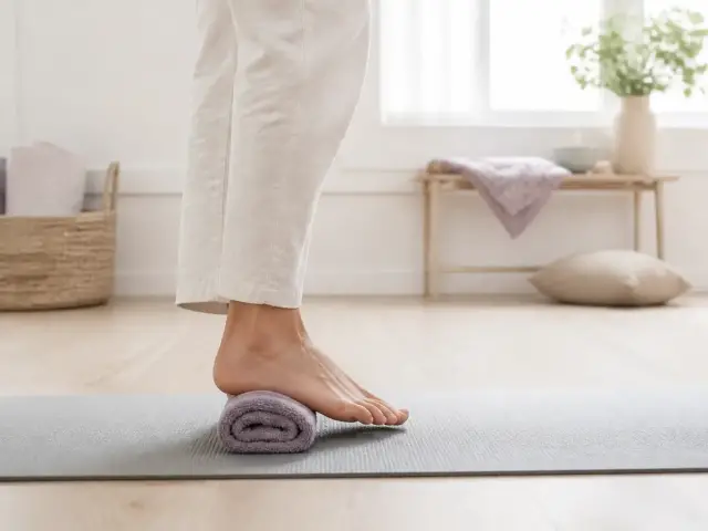 Pied nu posé sur un tapis de sol, vu de profil, talon en appui sur une serviette roulée