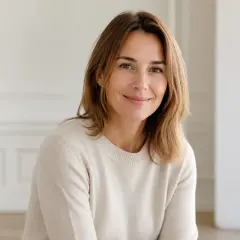 Portrait de Faustine Brunelle, cheveux châtains mi-longs, pull de laine crème, sourire léger, fond clair flou