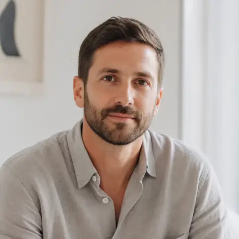 Portrait de Josselin Labbé, cheveux bruns courts, barbe courte, chemise de lin gris galet, fond clair flou