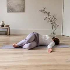 Personne allongée sur le dos sur un tapis, genoux pliés, la tête tournée sur le côté, dans une pièce calme