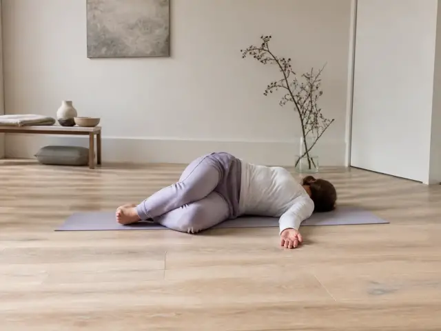 Personne allongée sur le dos sur un tapis, genoux pliés, la tête tournée sur le côté, dans une pièce calme
