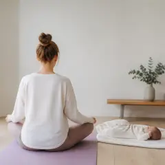 Femme assise en tailleur sur un tapis, vue de dos, un bébé allongé sur une couverture à côté d’elle